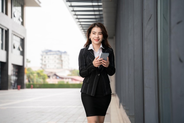 아시아 회사원은 대도시에서 스마트폰으로 친구와 정장을 입고 문자를 주고받으며 웃고 있습니다.
