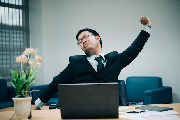 Asian officer man stretching body at the desk of office from back angleThailand peopleBusinessman tired from hard work