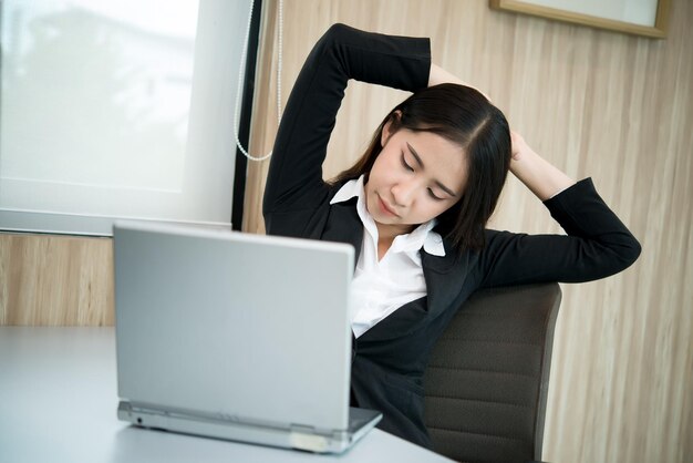 Asian officer woman stretching body at the desk of office from back angleThailand peopleBusinesswoman tired from hard work