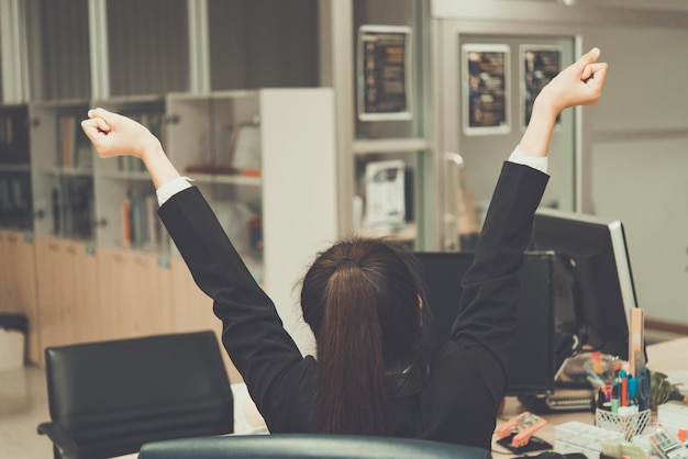 Asian officer woman stretching body at the desk of office from back angleThailand peopleBusinesswoman tired from hard work