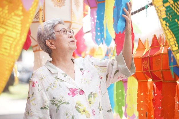 Азиатская пожилая пожилая женщина с висящим декоративным праздничным бумажным фонарем