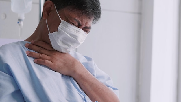 Asian old man is hospitalized with COVID19 Old male patient wearing a medical mask sits on the patient's bed