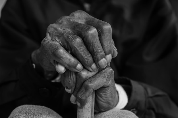 Asian old man sitting with his hands on a walking stick