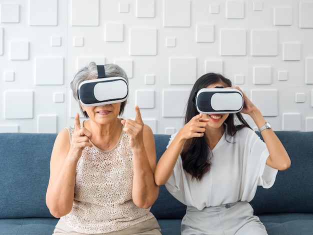 Asian old senior woman mother and happy young daughter female\
wearing vr glasses enjoy 3d game online together in white room mom\
and daughter with reality virtual technology lifestyle concept