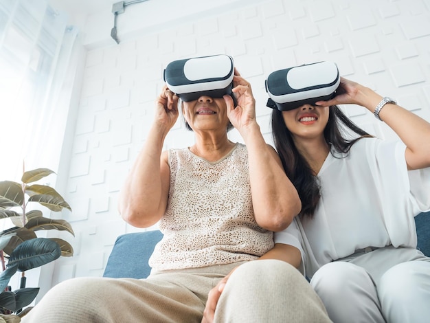 Asian old senior woman mother and happy young daughter female
wearing vr glasses enjoy 3d game online together in white room mom
and daughter with reality virtual technology lifestyle concept