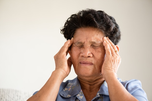 Asian old woman sitting on sofa and having a headache