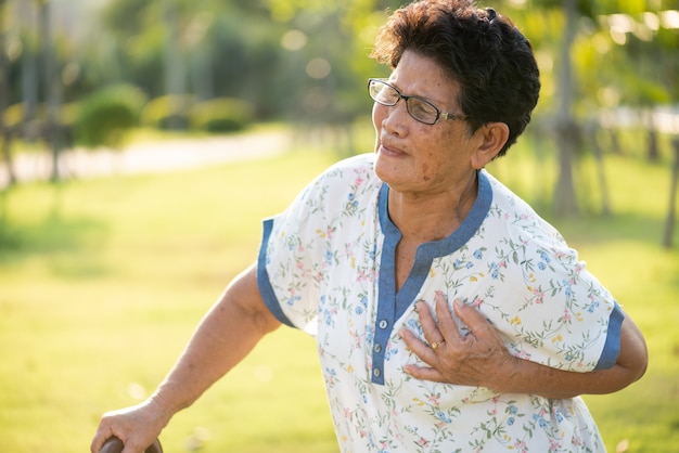 Donna anziana asiatica che cammina nel parco e che ha a con dolore sul cuore