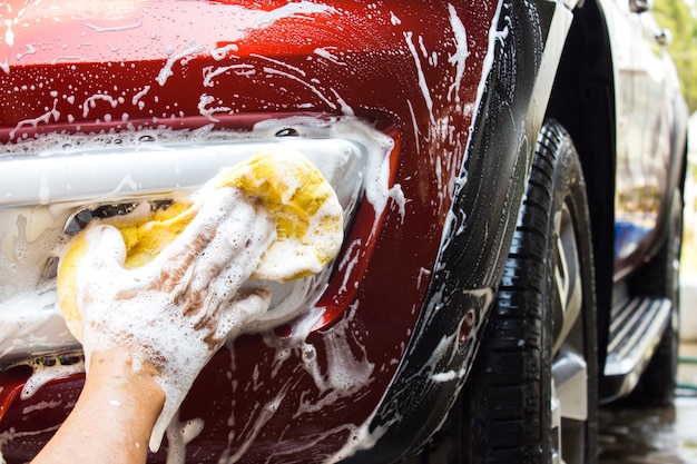 Asian oldman using yellow sponge washing front fog light of new red car. 