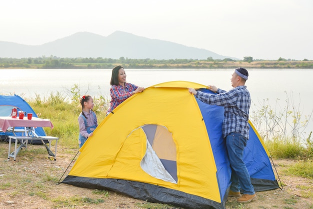 Asian parent with daughter setting tent by the lake. Family outdoor activity adventure on vacation.