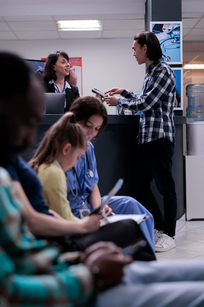 Asian patient at hospital front desk paying at pos using credit card for medical services at clinic. Young man after hospital visit typing pin number after making transaction for healthcare.