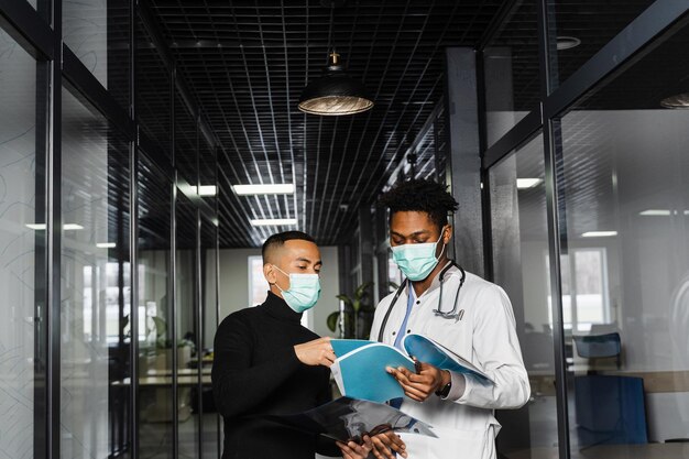 Asian patient with xrays asks an african doctor about treatment\
of pneumonia and pleurisy black surgeon consult and help asian\
man