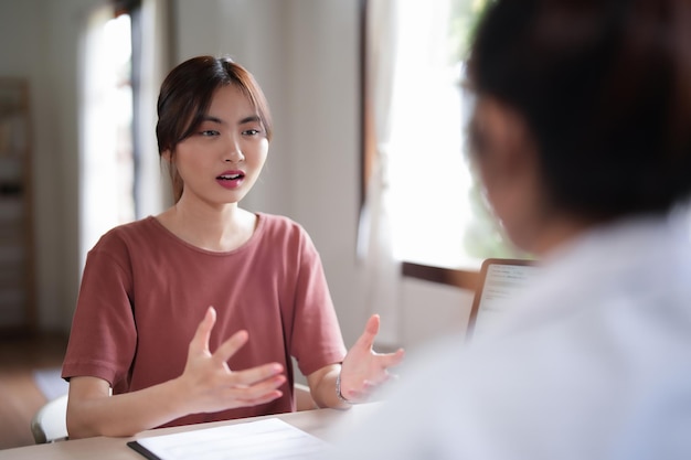 アジアの女性患者が不安でストレスを受け心理的健康問題について医者に説明し女性心理学者がメモを書き医学と精神健康療法についてカウンセリングしています