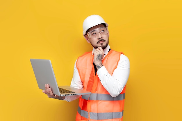 Asian pensive foreman in uniform holds laptop and thinks korean civil engineer