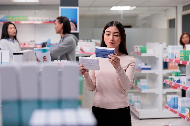 Asian person examining boxes of vitamins dispersed on shelves
in pharmacy, looking for prescription medicine and related
healthcare services. woman checking medicaments package
leaflet.