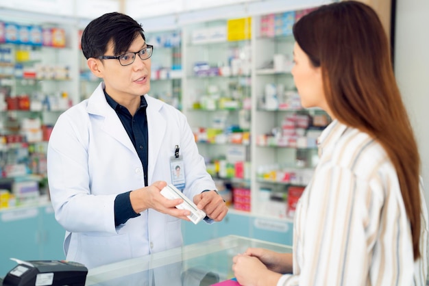 아시아 약사는 약국에서 고객에게 약과 약을 사용하는 방법을 설명합니다.