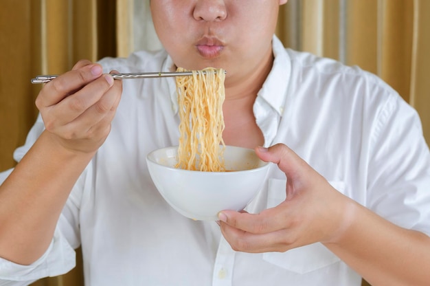 自宅でインスタントラーメンを食べるために銀の箸を使用して白いシャツを着たアジアのプラスサイズの男