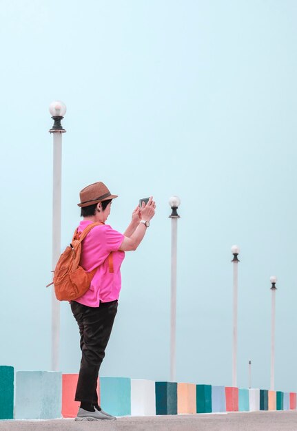 Asian plus size woman using smartphone to taking picture on multicolored bridge at sea viewpoint