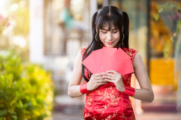 Asian Portrait transgender woman wearing red traditional Chinese cheongsam decoration holding red envelopes in hand at Chinese shrine for Chinese New Year