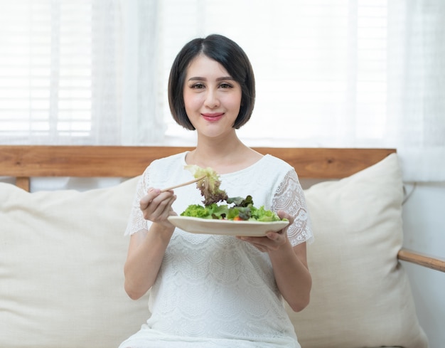 Asian pregnant woman holding green fresh salad on coach