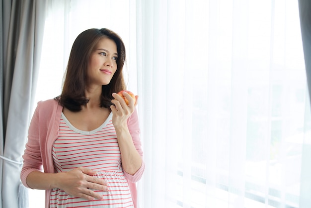 赤いリンゴを保持しているアジアの妊娠中の女性。