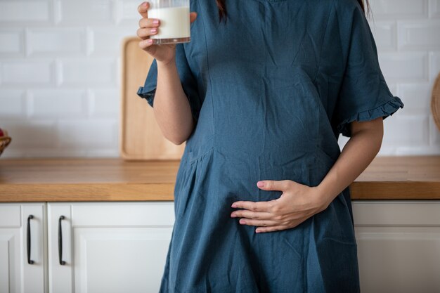 アジアの妊婦はミルクを飲んでいて、おなか、妊娠/出産に優しく触れています