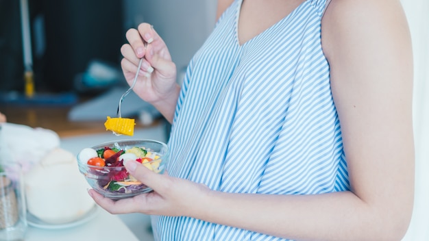 Asian pregnant woman is eating salad