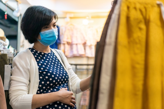 Photo asian pregnant woman wear face mask shopping for clothing in a boutique