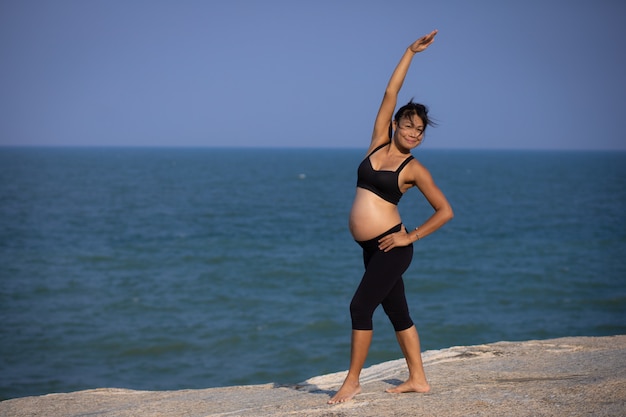 Asian pregnant woman yoga on the beach sunset summer time