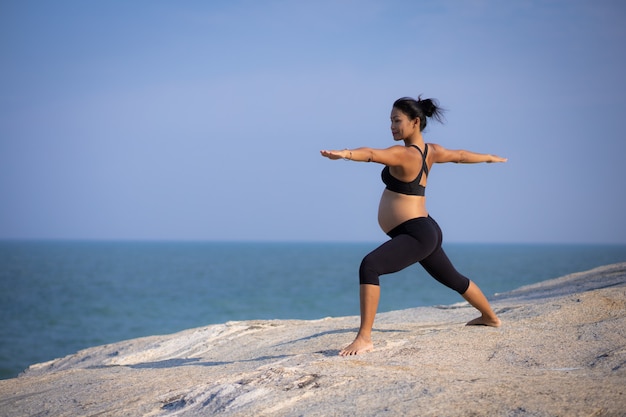 Asian pregnant woman yoga on the beach sunset summer time