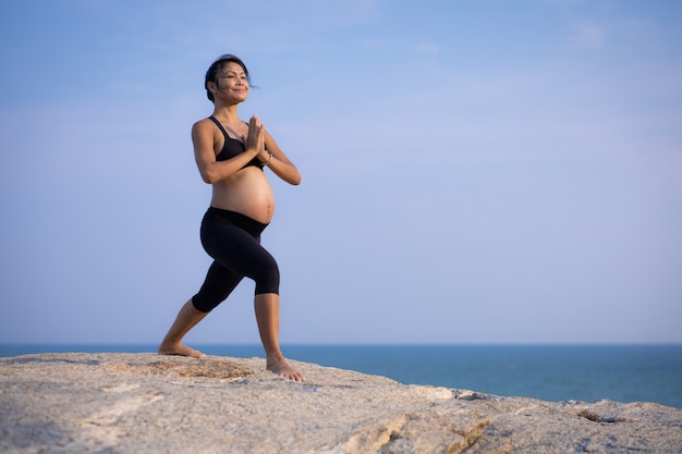 Asian pregnant woman yoga on the beach sunset summer time