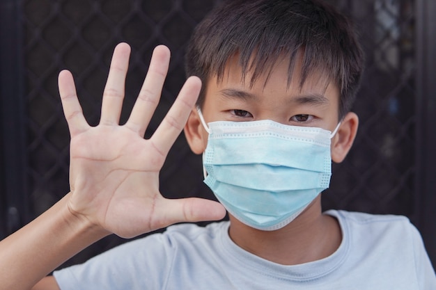 Asian preteen boy wearing medical face mask and making stop sign, self-quarantine,  coronavirus, covid-19 virus outbreak epidemic pandemic