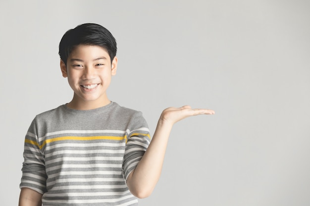 Asian preteen presenting something on hand over gray background.