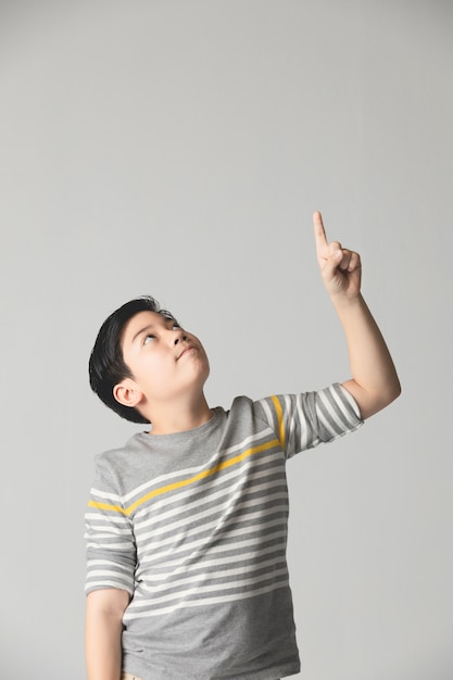 Asian preteen Teenage boy points up over gray background.