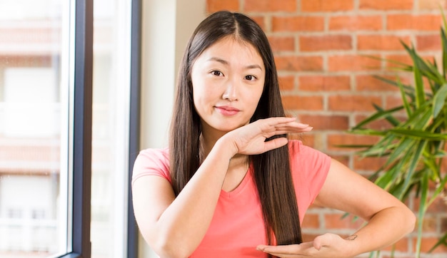 Asian pretty woman at home against brick wall with a plant