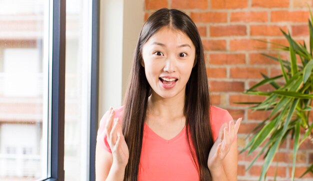 Asian pretty woman at home against brick wall with a plant