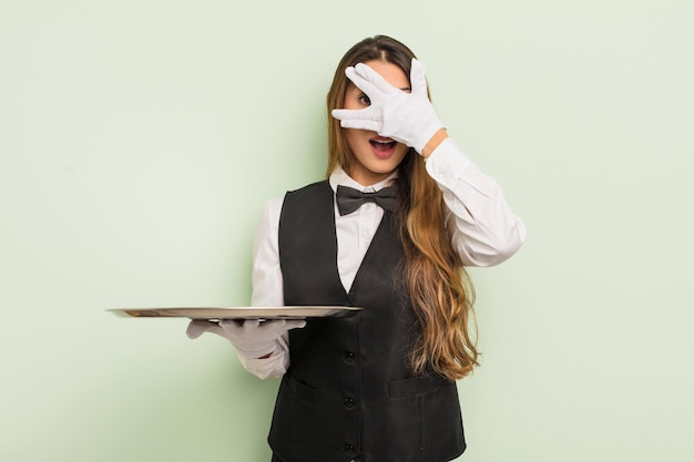 Photo asian pretty woman looking shocked, scared or terrified, covering face with hand. waiter and tray concept