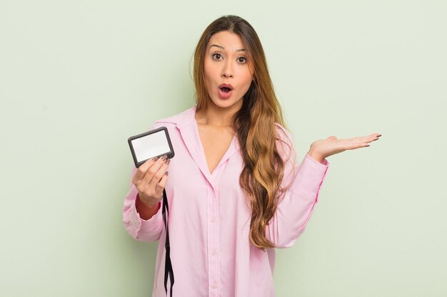 Asian pretty woman looking surprised and shocked with jaw dropped holding an object pass card id concept