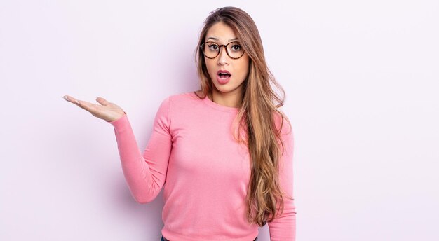 Asian pretty woman looking surprised and shocked, with jaw dropped holding an object with an open hand on the side