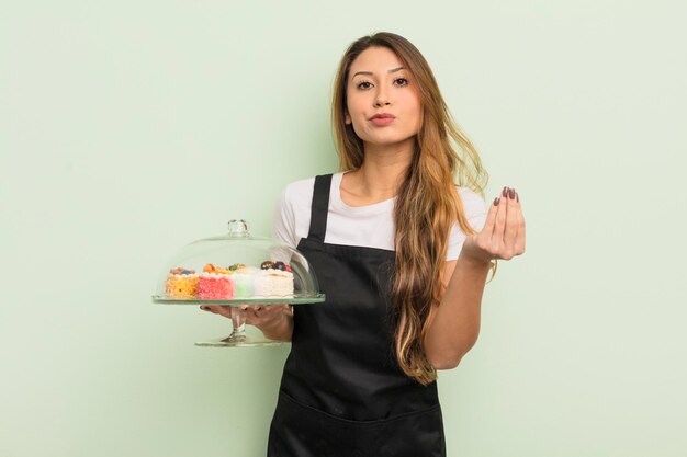 Asian pretty woman making capice or money gesture, telling you to pay. home made cakes concept