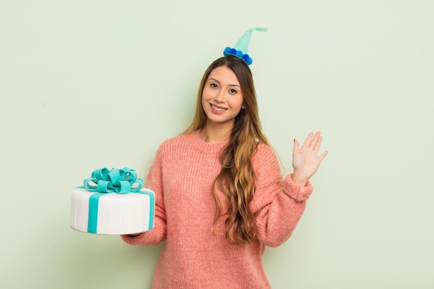 Donna graziosa asiatica sorridente felicemente agitando la mano dando il benvenuto e salutandoti concetto di compleanno