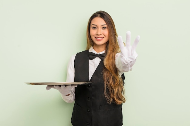 Asian pretty woman smiling and looking friendly, showing number three. waiter and tray concept