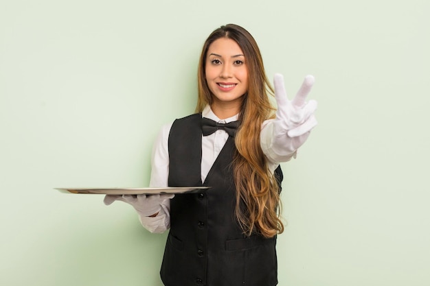 Foto donna graziosa asiatica sorridente e dall'aspetto amichevole che mostra il concetto di cameriere e vassoio numero due