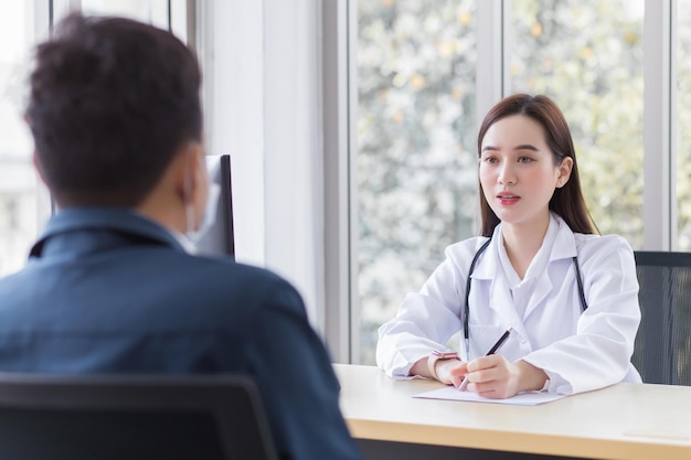 Asian professional woman doctor who wears medical coat talks with a man patient to consult