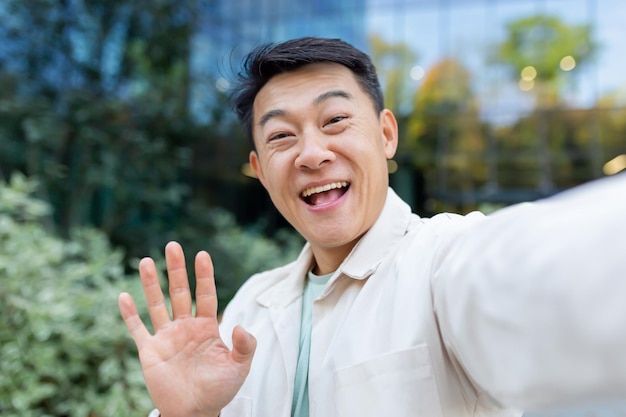 Asian programmer talking on video call using app on phone view camera man waving and talking