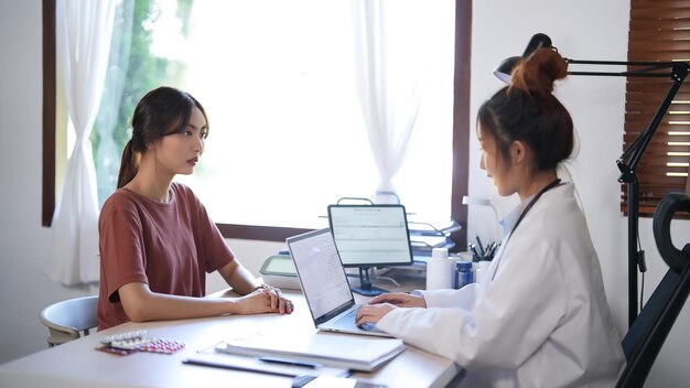 Asian psychologist women giving help and support to counseling about medicine and mental health therapy to female patient while working to typing medical data and prescription on laptop in clinic