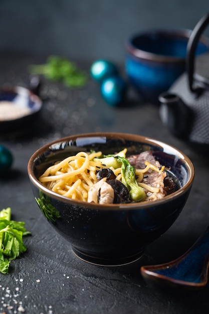 Asian ramen noodles soup with beef oyster mushrooms and vegetables in bowl on dark background