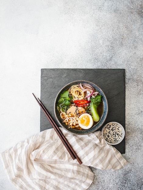 Asian Ramen noodles with chicken, pak choi cabbage and egg on a black slate board 