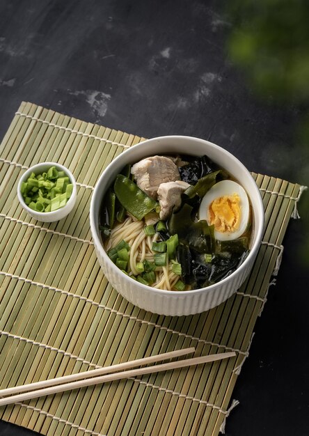 Asian ramen soup with chicken and egg noodles with the addition\
of fresh onions on a dark copyspace surface for menus and articles\
with recipes