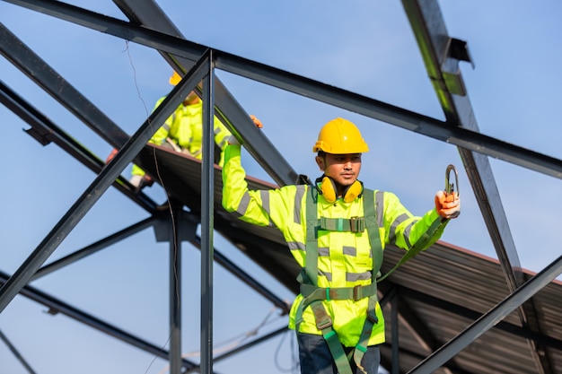 아시아 지붕 건설 노동자는 지붕 프레임을 설치하기 위해 안전 높이 장비를 착용하고, 건설 현장에서 안전 바디 하네스 후크가있는 작업자를위한 추락 방지 장치를 설치합니다.