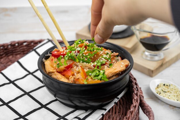 Asian salad with rice noodles, vegetables, mushrooms, chicken and soy sauce. Funchose with white transparent noodles in black plate